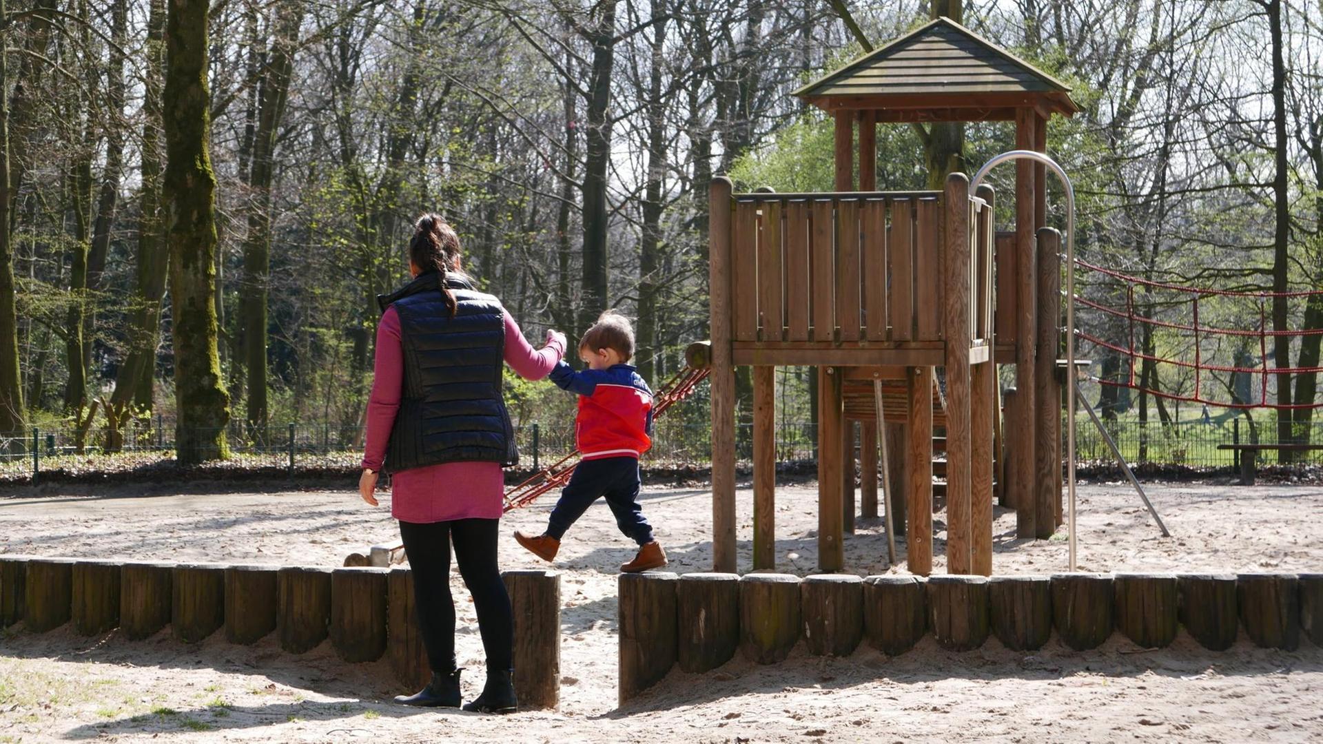Eine Frau hält einen Jungen an der Hand während er auf einer Brüstung auf dem Spielplatz balanciert. Eine Frau hält einen Jungen an der Hand während er auf einer Brüstung auf dem Spielplatz balanciert.