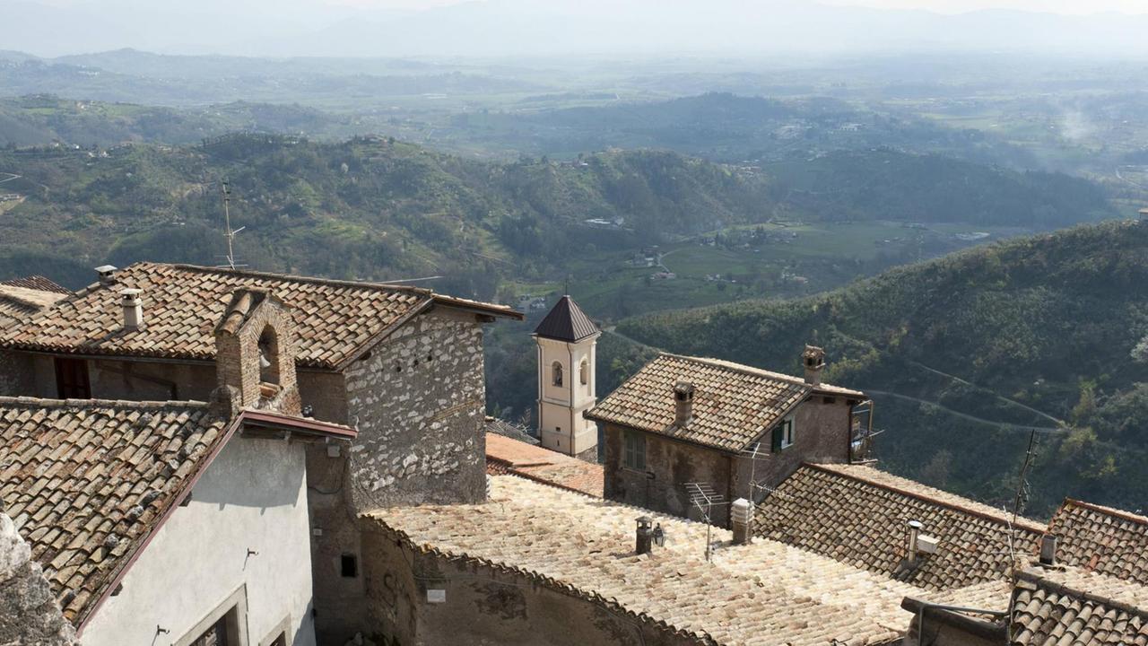 Blick über die historischen Ziegeldächer einer am Hang gelegenen Altstadt mit großzügiger Aussicht in eine grüne Hügellandschaft, die kaum besiedelt ist.