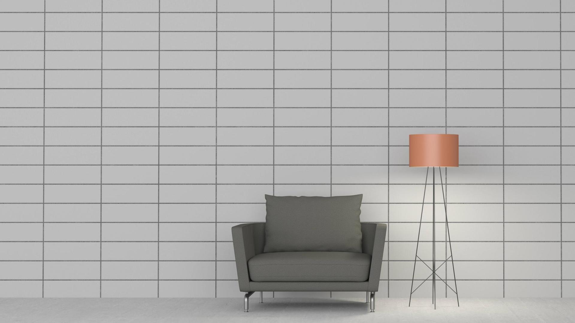 Ein schlichter grauer Sessel und eine filigrane Stehlampe vor einer Wand