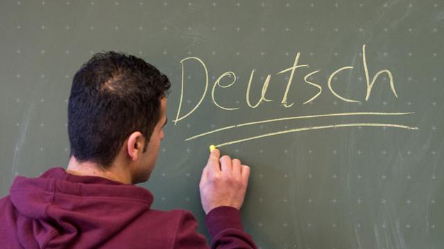 Ein Asylbewerber schreibt in einer Städtischen Berufsschule in Regensburg (Bayern) das Wort "Deutsch" an die Tafel.