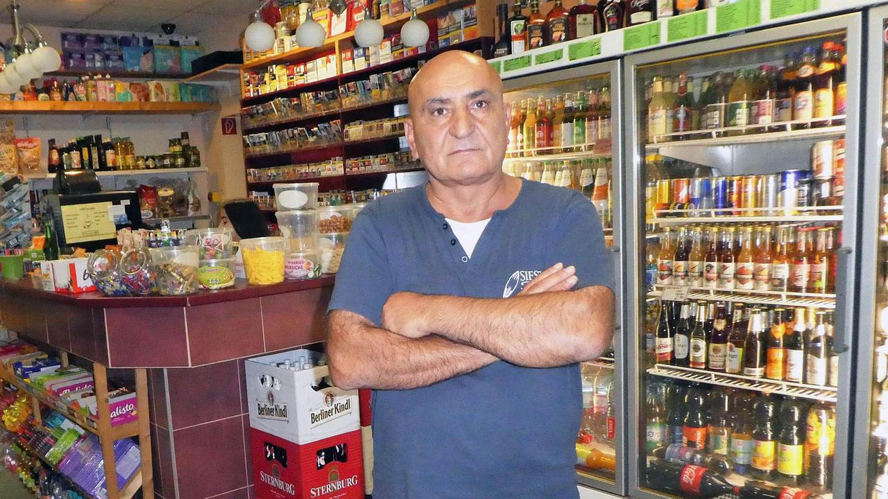 Porträt des Späti-Betreibers Hassan, ein glatzköpfiger, mittelalter Mann, vor seinem Getränkesortiment Porträt des Späti-Betreibers Hassan, ein glatzköpfiger, mittelalter Mann, vor seinem Getränkesortiment