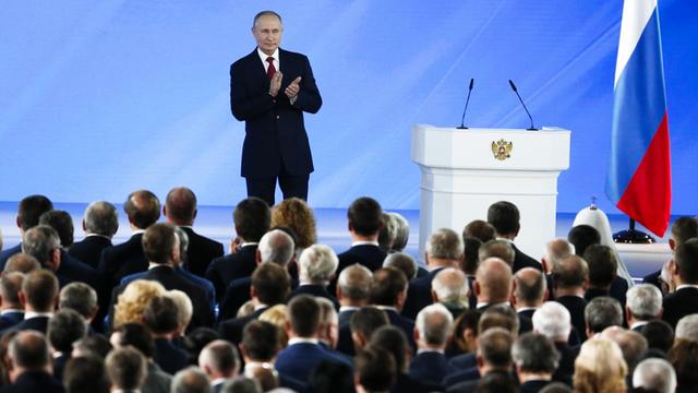 Der russische Präsident Putin steht auf einer Bühne und applaudiert. Vor ihm stehen viele Menschen.