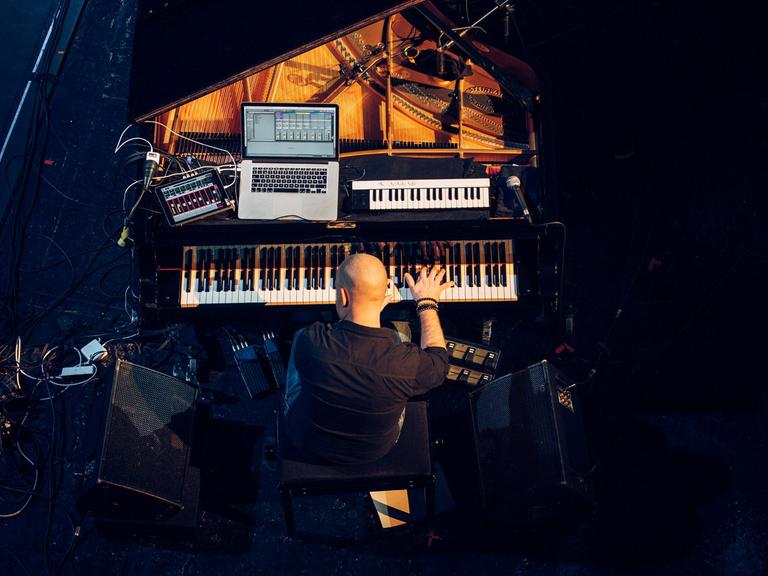 Der schwedische Pianist und Komponist Jakob Karlzon an seinem Arbeitsplatz, dem Flügel, auf dem auch noch Keyboard und Computer stehen.