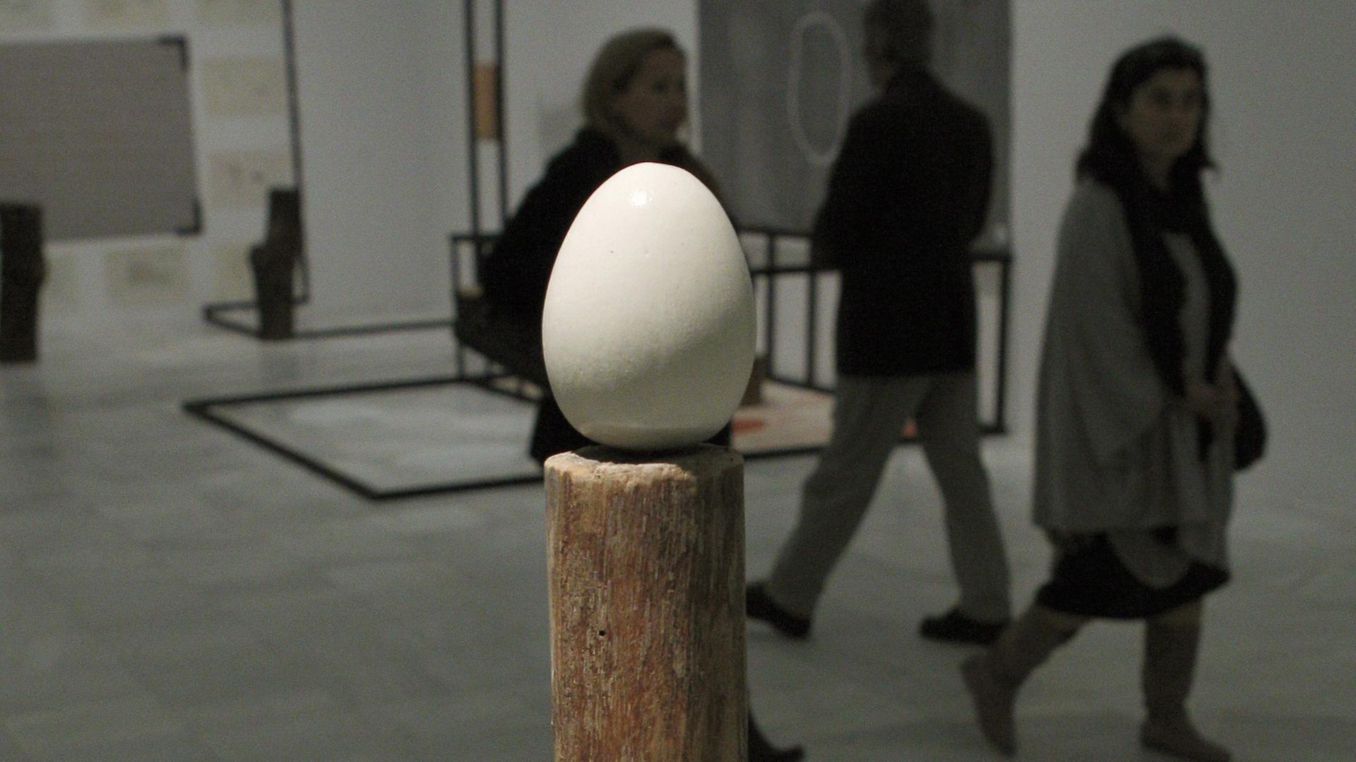 Die Skulptur "Stake and Egg" von Terry Fox, im Hintergrund laufen drei Besucher vorbei, die man nur als Schatten erkennt. Die Skulptur "Stake and Egg" von Terry Fox, im Hintergrund laufen drei Besucher vorbei, die man nur als Schatten erkennt.