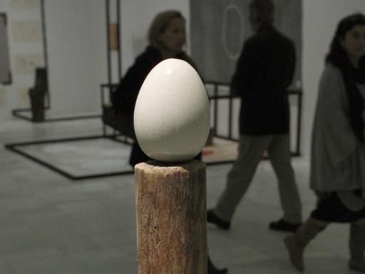 Die Skulptur "Stake and Egg" von Terry Fox, im Hintergrund laufen drei Besucher vorbei, die man nur als Schatten erkennt.