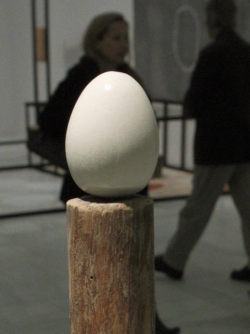 Die Skulptur "Stake and Egg" von Terry Fox, im Hintergrund laufen drei Besucher vorbei, die man nur als Schatten erkennt.