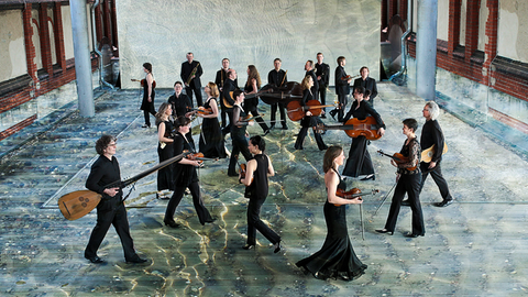 Das Ensemble Lautten Compagney läuft mit Instrumenten in schwarzer Konzertkleidung durch eine Halle