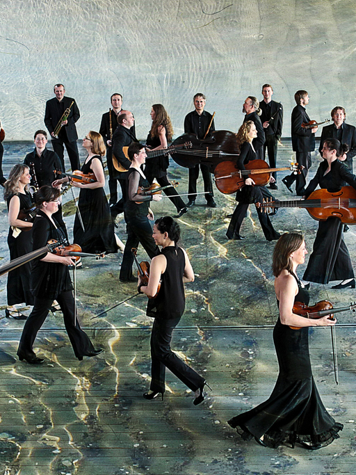 Das Ensemble Lautten Compagney läuft mit Instrumenten in schwarzer Konzertkleidung durch eine Halle