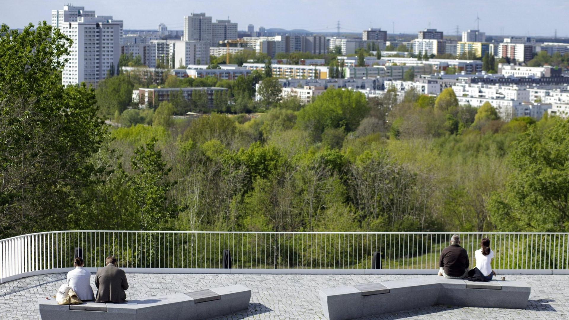 Zwei Paare sitzen am Stadtrand jeweils auf einer Bank mit viel Abstand zueinander und blicken auf die Stadt Berlin in der Ferne. Zwei Paare sitzen am Stadtrand jeweils auf einer Bank mit viel Abstand zueinander und blicken auf die Stadt Berlin in der Ferne.