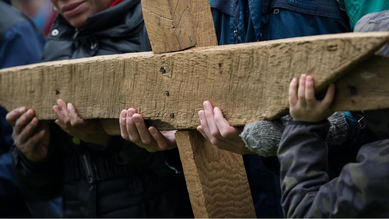 Gläubige halten bei einer ökumenischen Kreuzwegprozession am Karfreitag gemeinsam ein großes Holzkreuz. Gläubige halten bei einer ökumenischen Kreuzwegprozession am Karfreitag gemeinsam ein großes Holzkreuz.