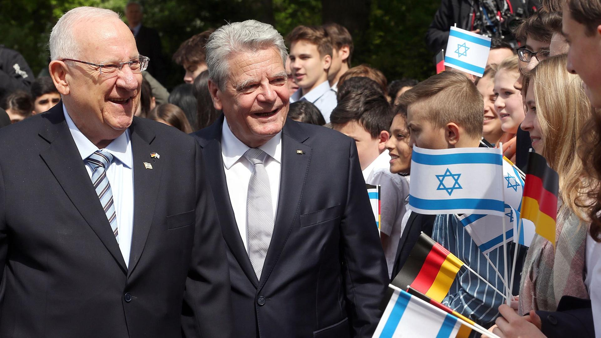 Bundespräsident Gauck (r) empfängt den israelischen Präsidenten Rivlin, daneben Jugendliche mit deutschen und israelischen Fahnen.