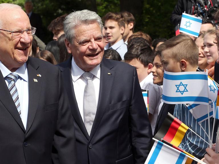 Bundespräsident Gauck (r) empfängt den israelischen Präsidenten Rivlin, daneben Jugendliche mit deutschen und israelischen Fahnen.