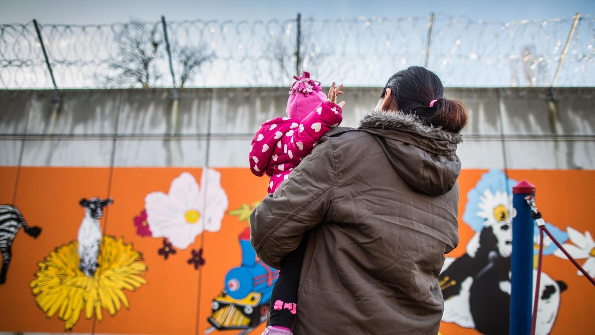 Eine Gefangene steht in Frankfurt am Main in einer Justizvollzugsanstalt mit ihrer kleinen Tochter auf dem Arm vor der bunt bemalten Gefängnismauer. Eine Gefangene steht in Frankfurt am Main in einer Justizvollzugsanstalt mit ihrer kleinen Tochter auf dem Arm vor der bunt bemalten Gefängnismauer.
