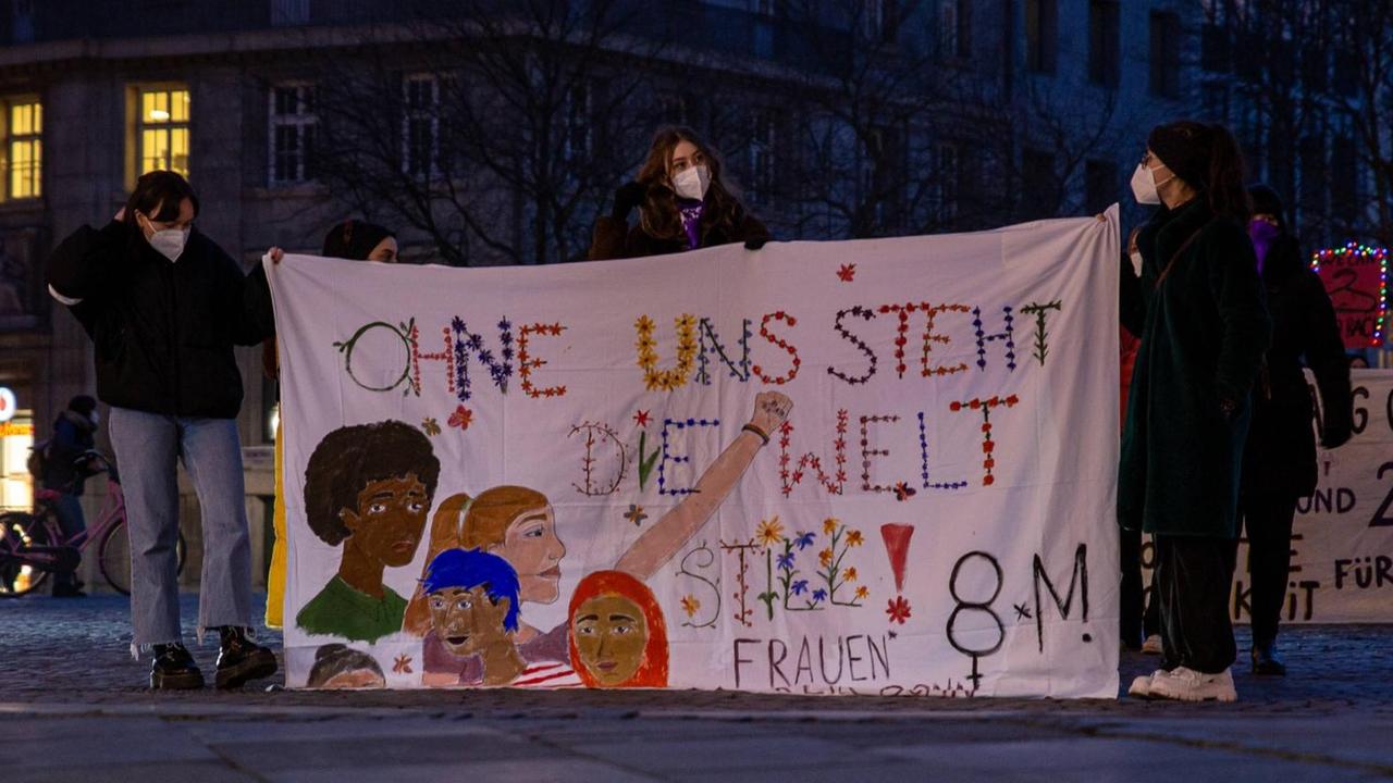 Frauen halten ein Plakat hoch. Darauf steht: Ohne uns steht die Welt still.