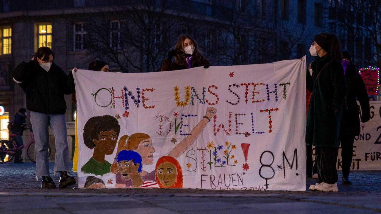 Frauen halten ein Plakat hoch. Darauf steht: Ohne uns steht die Welt still. Frauen halten ein Plakat hoch. Darauf steht: Ohne uns steht die Welt still.