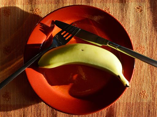 Besteck und eine Banane liegen auf einem orangefarbenen Teller.