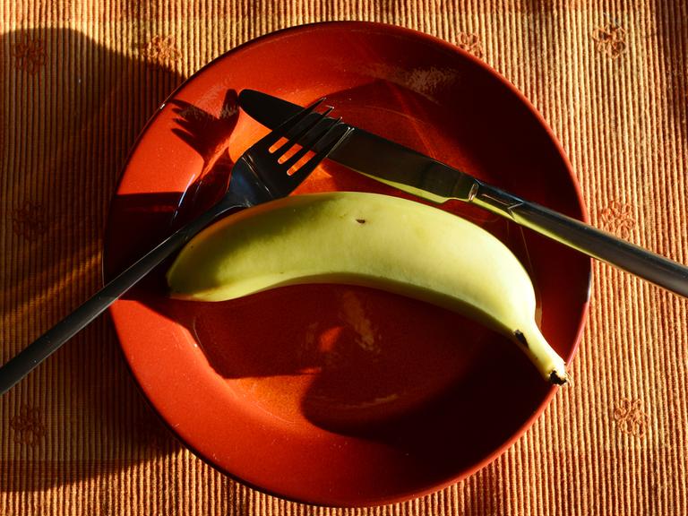 Besteck und eine Banane liegen auf einem orangefarbenen Teller.