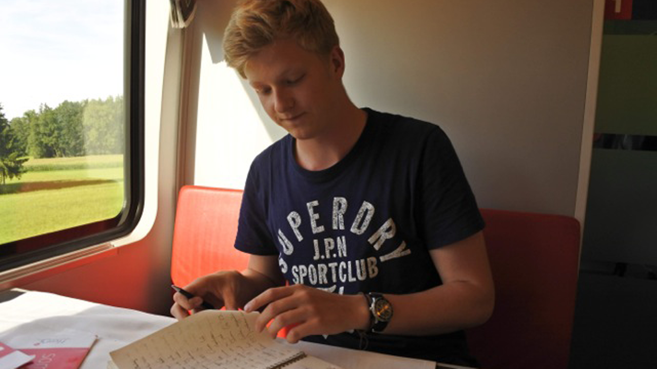 Leon Morelli mit Reisetagebuch. Morelli sitzt im Zug. 
