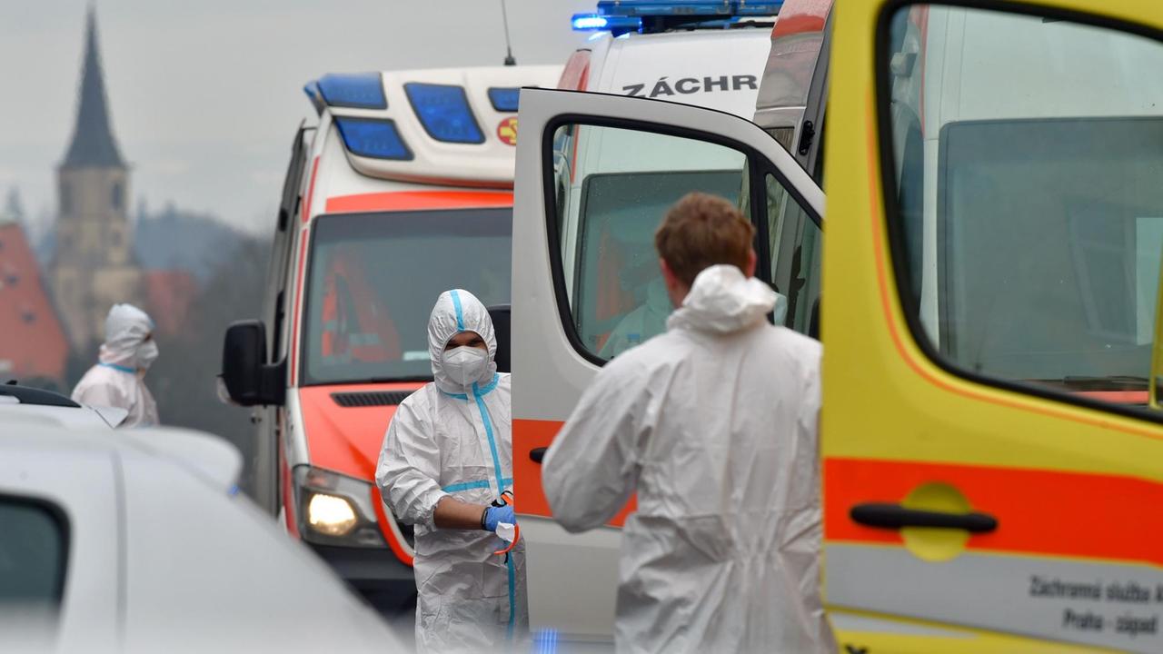 Cheb: Medizinische Mitarbeiter tragen Schutzkleidung und stehen vor Krankenwagen. 