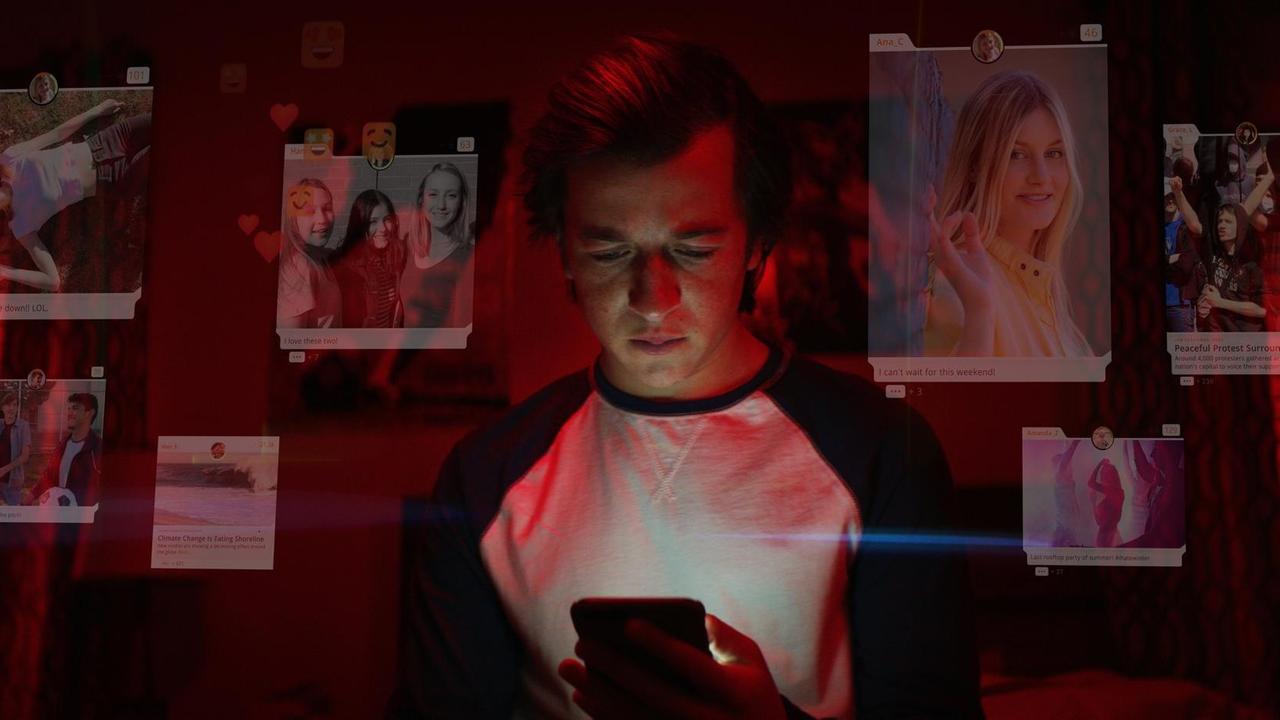Ein junger Mann schaut auf sein Smartphone, um ihn herum sind leicht verblasst Posts aus sozialen Netzwerken zu sehen. Ein junger Mann schaut auf sein Smartphone, um ihn herum sind leicht verblasst Posts aus sozialen Netzwerken zu sehen.