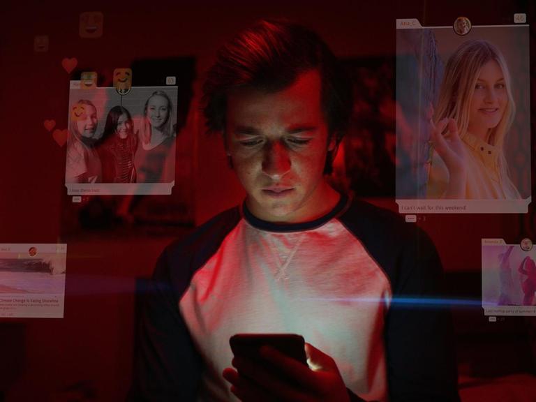 Ein junger Mann schaut auf sein Smartphone, um ihn herum sind leicht verblasst Posts aus sozialen Netzwerken zu sehen.