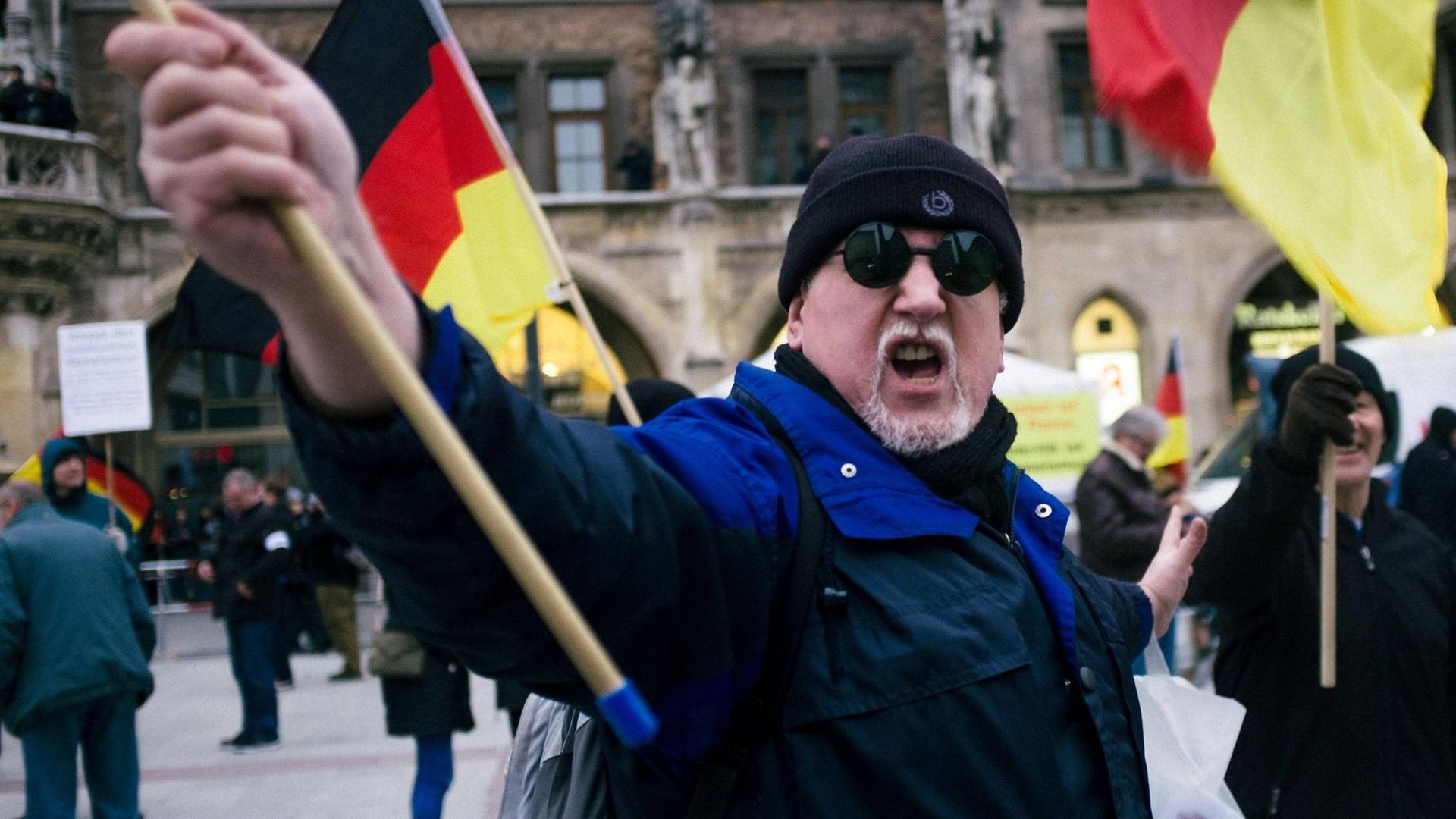 Ein vermummter Pegida-Demonstrant schwenkt eine Deutschland-Fahne. Ein vermummter Pegida-Demonstrant schwenkt eine Deutschland-Fahne.