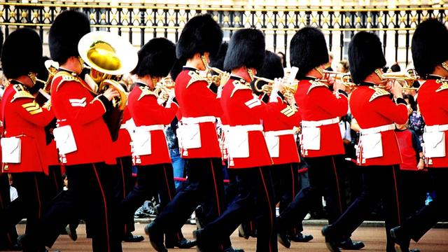 Die Königliche Garde vor dem Buckingham Palace bei der Wachablösung. Soldaten marschieren, spielen Blasinstrumente, tragen Bärenfellmützen