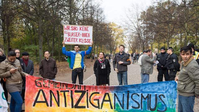 "Gemeinsam Antiziganismus bekämpfen" steht auf einem Banner, das mehrere Menschen vor dem Mahnmal für Sinti und Roma in Berlin bei einer Kundgebung festhalten.