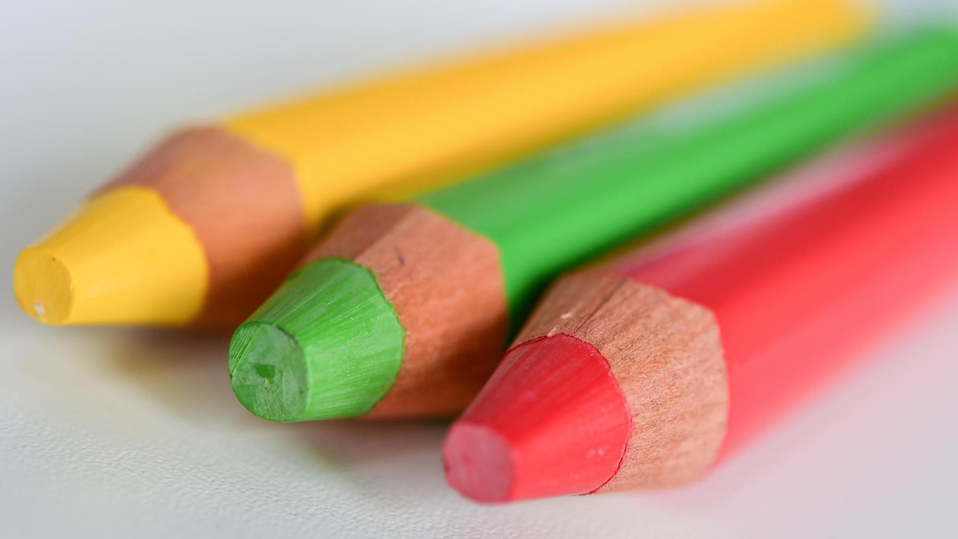 Drei Farbstifte in den Farben Rot, Grün und Gelb liegen nebeneinander Drei Farbstifte in den Farben Rot, Grün und Gelb liegen nebeneinander