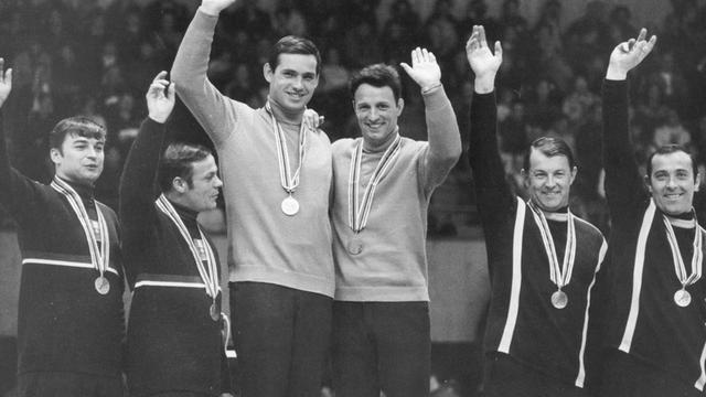 Der schnellste Doppelsitzer der Olympischen Winterspiele in Grenoble wird am 18.02.1968 im Eispalast der Stadt mit der Goldmedaille geehrt: Das DDR-Rodel-Duo Thomas Köhler (4.v.l.) und Klaus Bonsack (3.v.l) sichert sich die Goldmedaille vor den Österreichern Manfred Schmid, Ewald Walch (l) und den bundesdeutschen Rennrodlern Wolfgang Winkler/Fritz Nachmann (r)