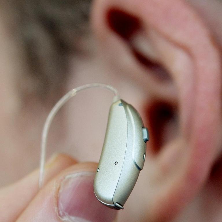 Ein Mitarbeiter hält am 19.12.2014 bei einem Hörgeräteakustiker in Stuttgart zur Demonstration ein Hörgerät vor sein Ohr. 