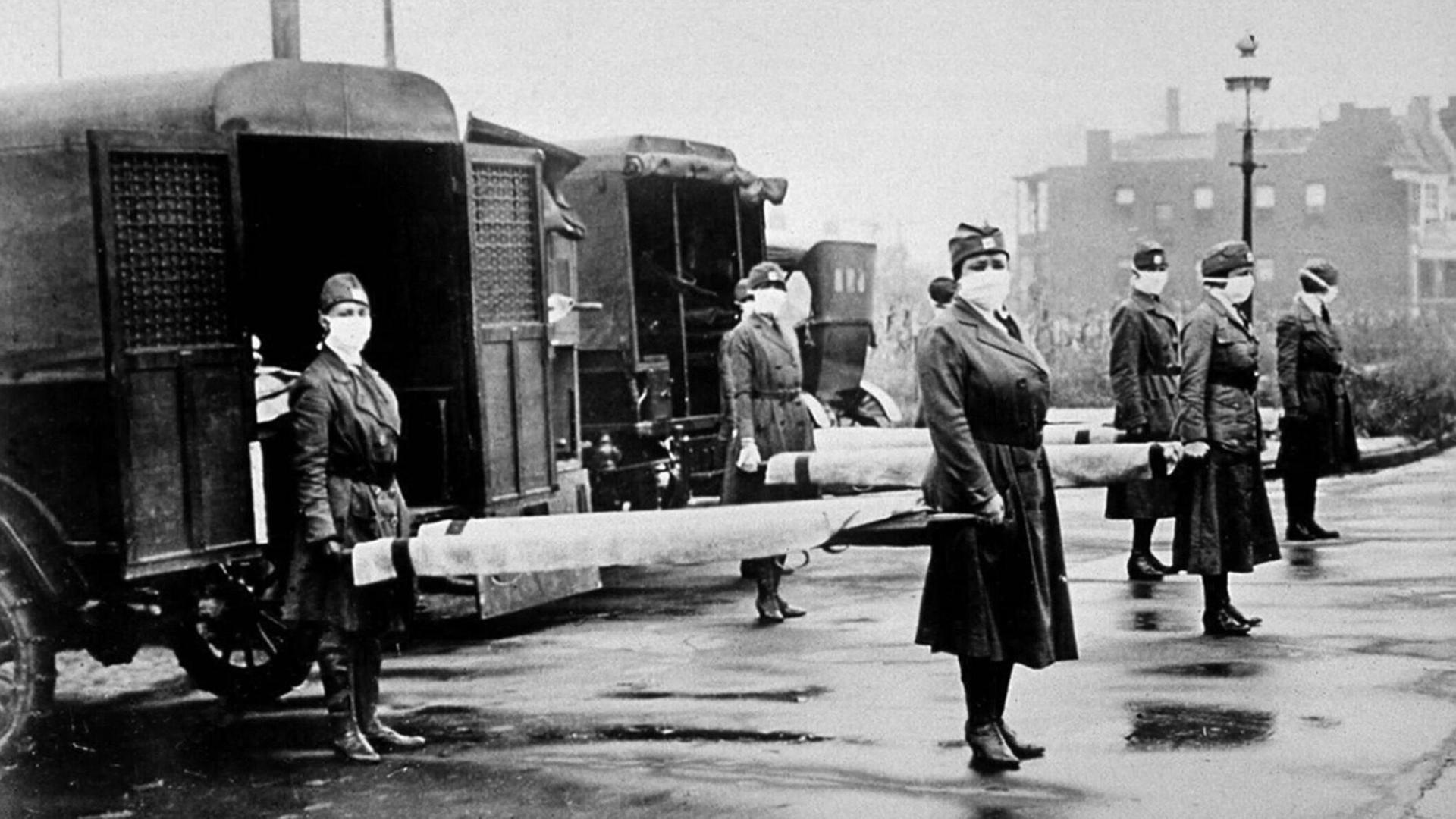 Foto aus dem Winter 1918/19: Krankenschwestern mit Mundschutz stehen mit Bahren vor Krankenwagen.