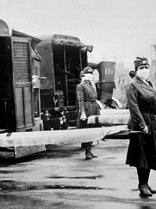 Foto aus dem Winter 1918/19: Krankenschwestern mit Mundschutz stehen mit Bahren vor Krankenwagen.