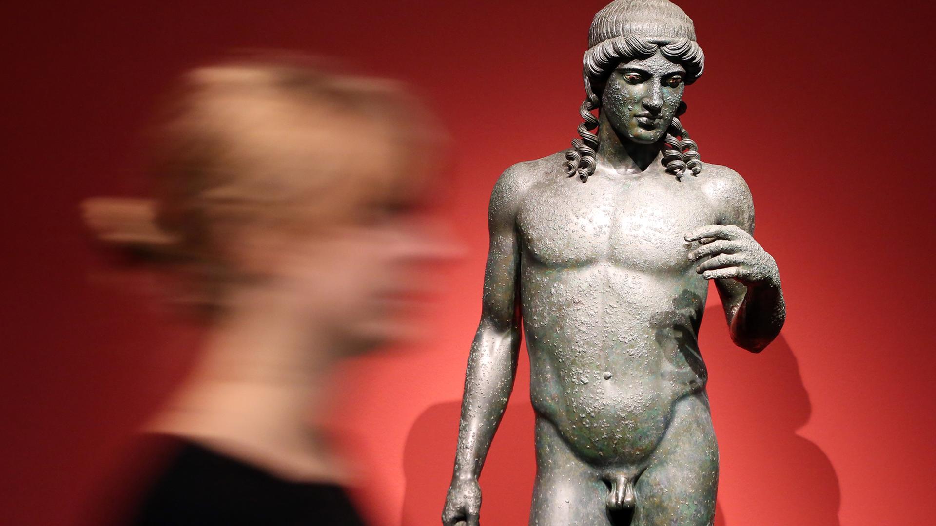Eine Frau geht in der Ausstellung "Pompeji - Götter, Mythen, Menschen" im Bucerius Kunst Forum in Hamburg an der "Statue des Apollon" entlang.
