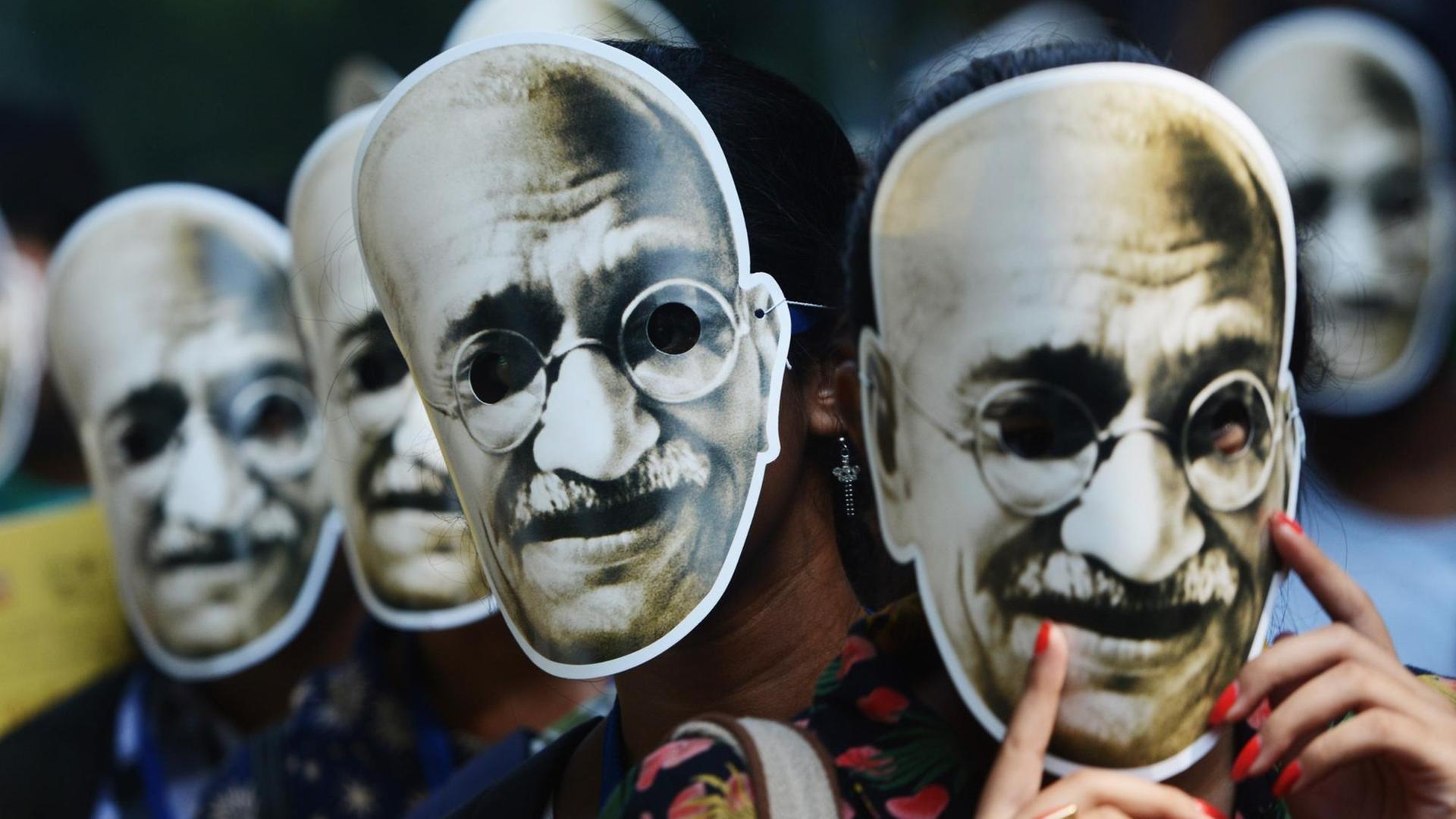 Pappmasken von Ghandi werden von unterschiedlichen Menschen auf der Straße getragen.