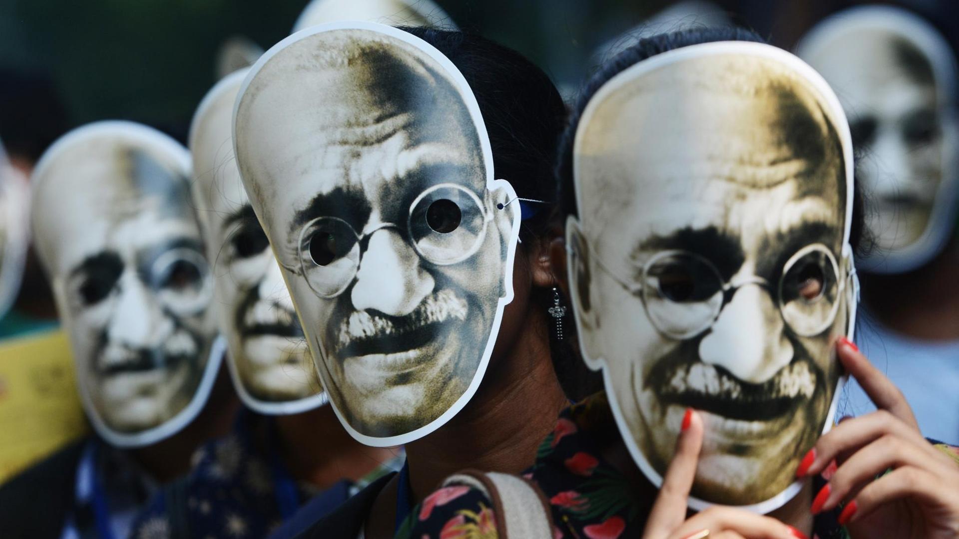 Pappmasken von Ghandi werden von unterschiedlichen Menschen auf der Straße getragen. Pappmasken von Ghandi werden von unterschiedlichen Menschen auf der Straße getragen.