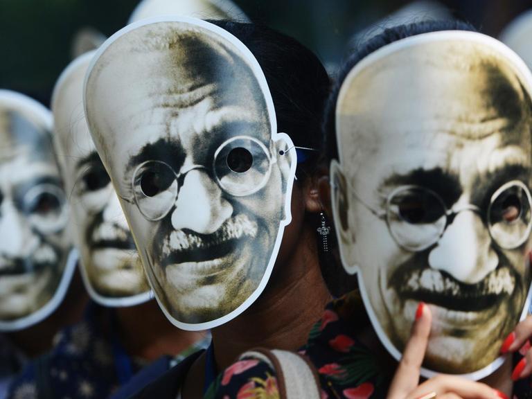 Pappmasken von Ghandi werden von unterschiedlichen Menschen auf der Straße getragen.