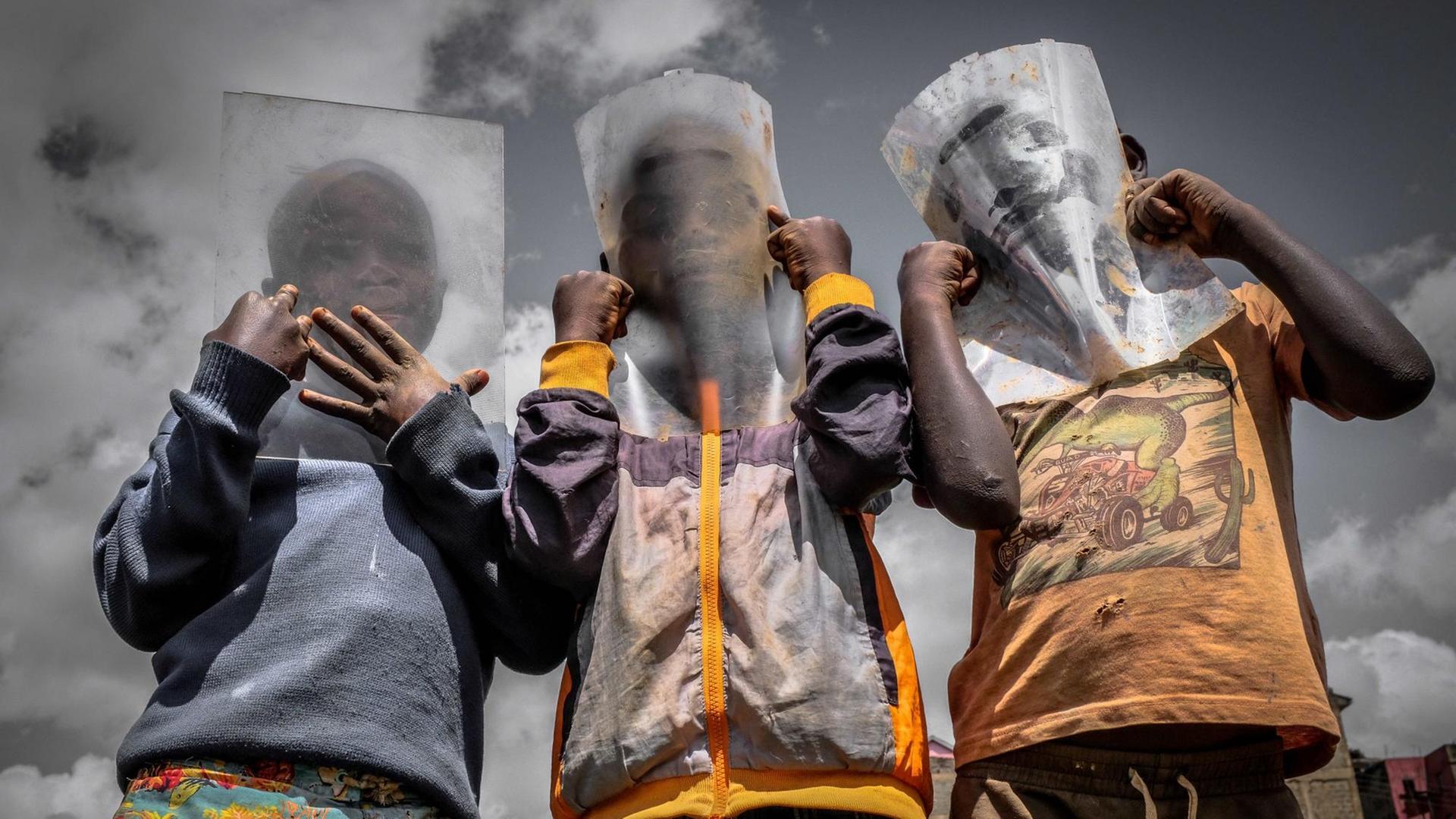Drei Jungen halten sich eine Plastikfolie vor's Gesicht, weil sie keine Atemschutzmaske kaufen können.