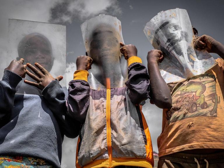 Drei Jungen halten sich eine Plastikfolie vor's Gesicht, weil sie keine Atemschutzmaske kaufen können.
