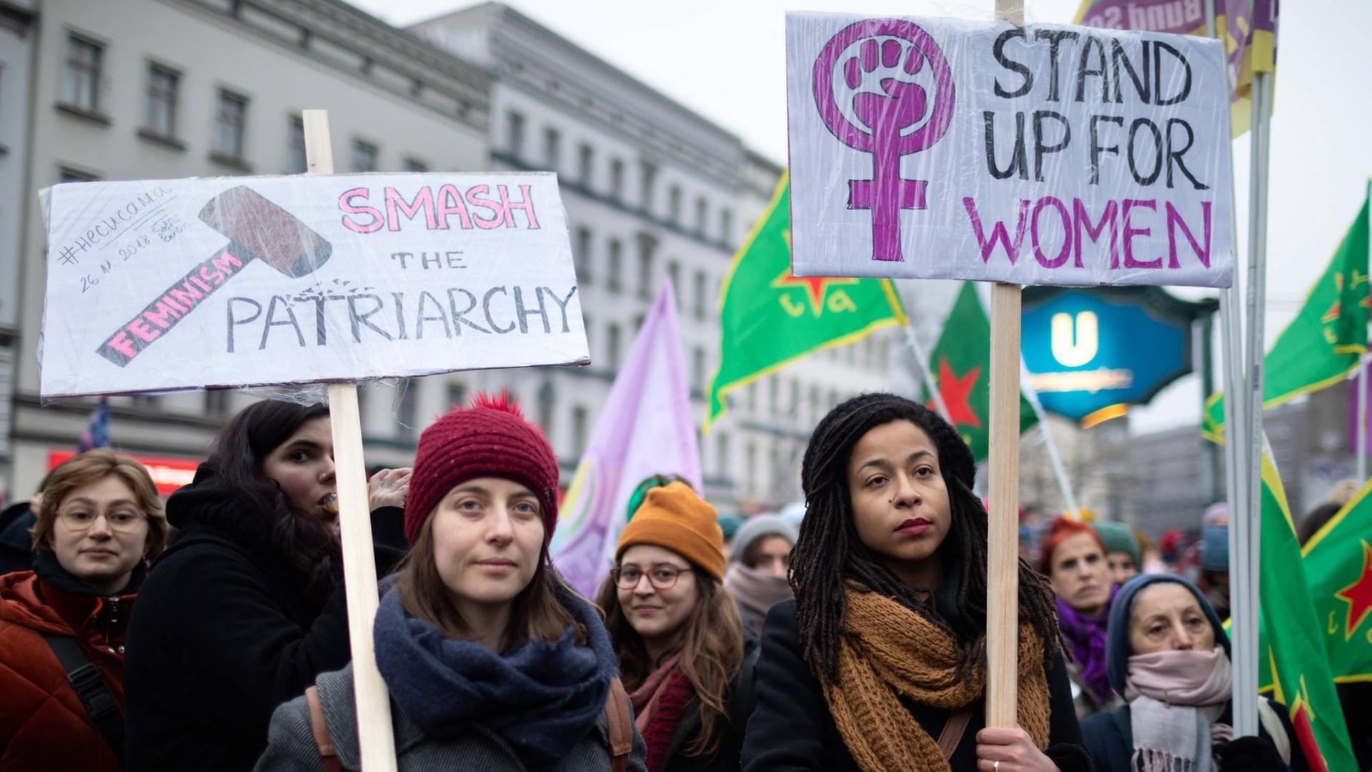 Zwei Frauen halten Plakate, auf denen steht "Smash the Patriarchy" und "Stand up for Women" Zwei Frauen halten Plakate, auf denen steht "Smash the Patriarchy" und "Stand up for Women"