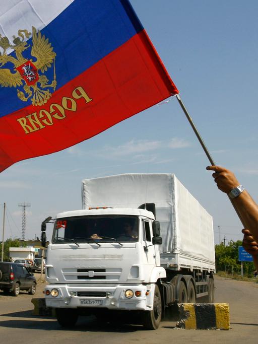 Ein Mann schwenkt eine russische Fahne, im Hintergrund ist ein weißer Lkw des umstrittenen russischen Hilfskonvois für die Ukraine zu sehen.