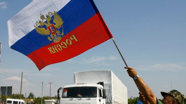 Ein Mann schwenkt eine russische Fahne, im Hintergrund ist ein weißer Lkw des umstrittenen russischen Hilfskonvois für die Ukraine zu sehen.