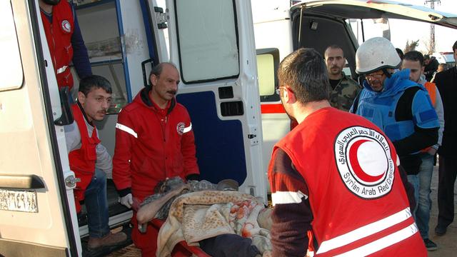 Helfer des Roten Halbmonds evakuieren in Syrien weitere Menschen aus der vom Bürgerkrieg stark betroffenen Stadt Homs Zwei Männer tragen eine Bahre in einen Rettungswagen.