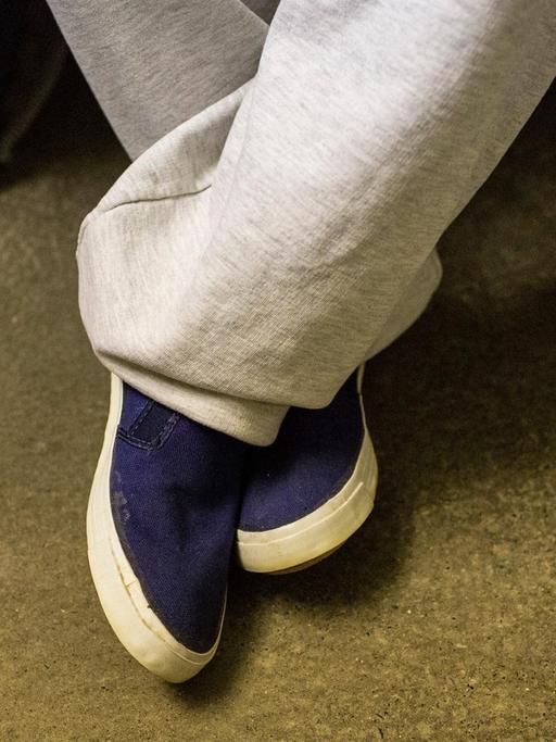 Nahaufnahme der Beine und Schuhe eines Gefangenen in seiner Zelle.