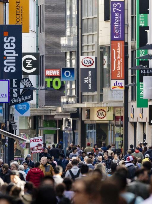 Passanten auf der Hohe Straße in Köln, im Hintergrund sind die Schilder vieler Geschäfte zu sehen