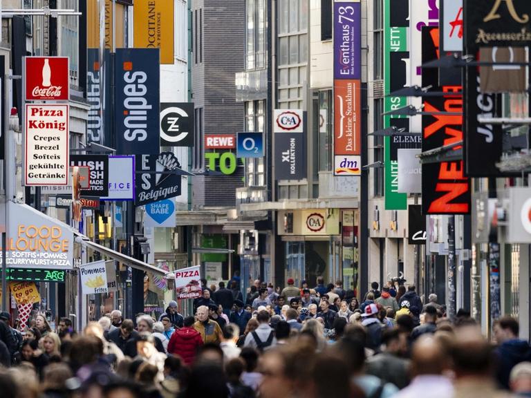 Passanten auf der Hohe Straße in Köln, im Hintergrund sind die Schilder vieler Geschäfte zu sehen