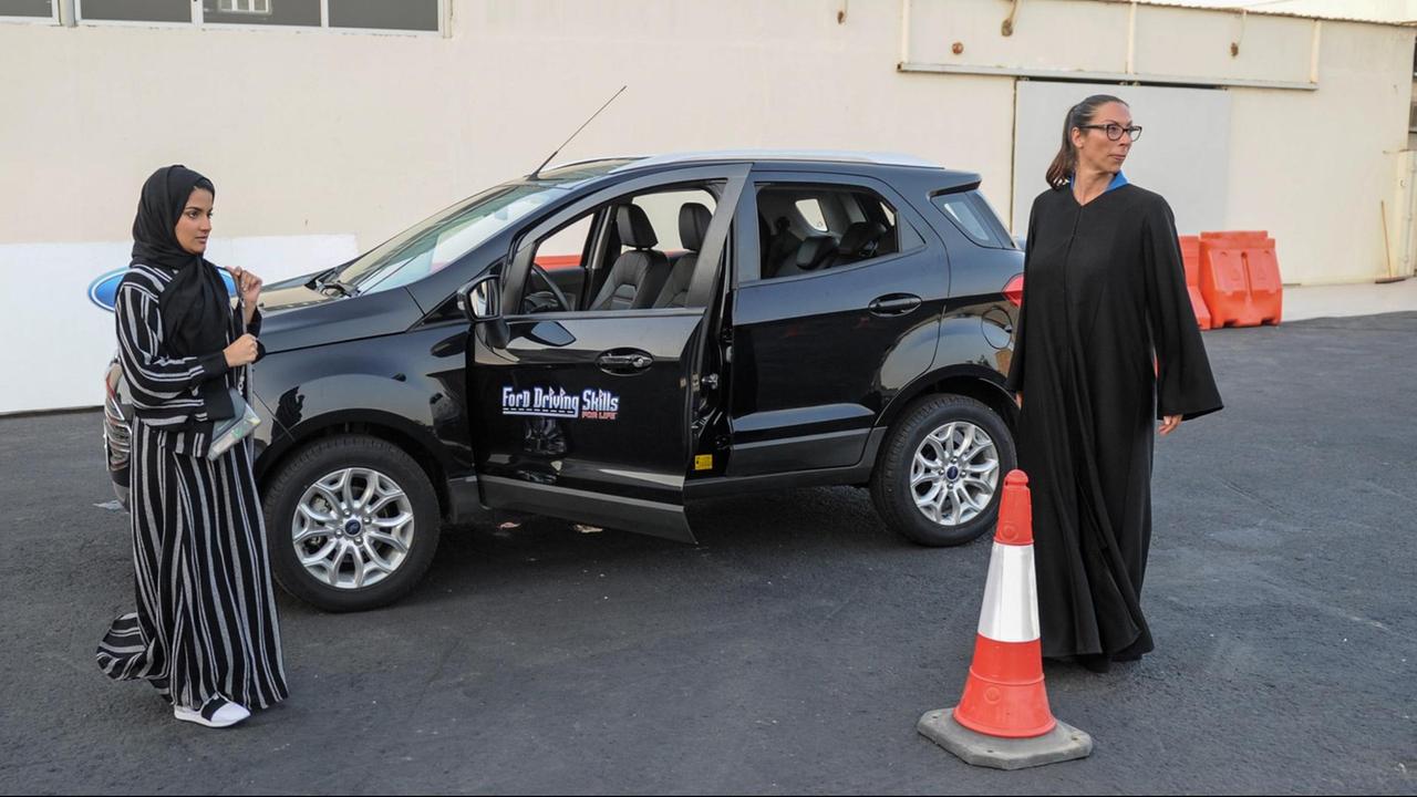 Eine saudi-arabische Frau in Jeddah steht mit ihrer italienischen Fahrlehrerin vor einem schwarzen Auto und erhält Anweisungen Eine saudi-arabische Frau in Jeddah steht mit ihrer italienischen Fahrlehrerin vor einem schwarzen Auto und erhält Anweisungen