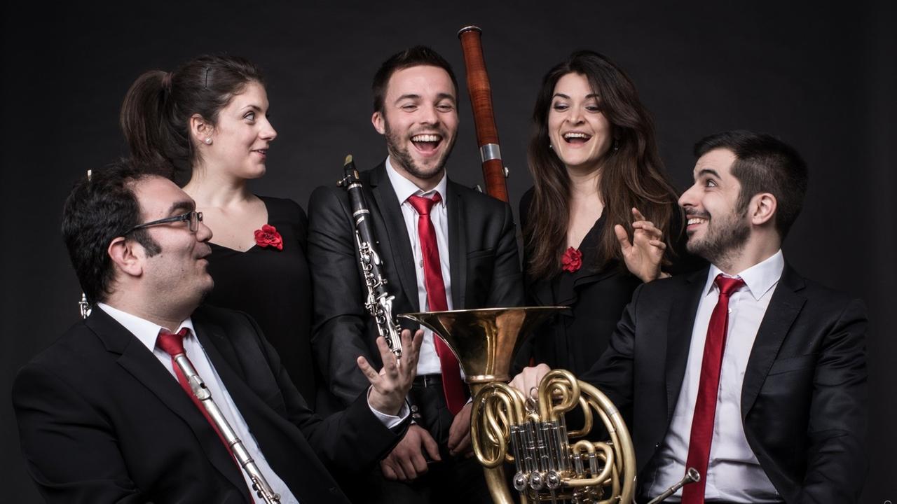 Fünf Musiker und Musikerinnen stehen mit ihren Instrumenten eng beieinander und lachen sich gegenseitig an.