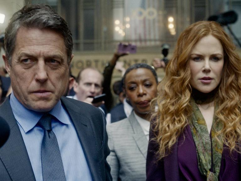 Szene aus der Serie "The Undoing" mit dem Schauspieler Hugh Grant als Jonathan Fraser und der Schauspielerin Nicole Kidman als Grace Fraser. Ein Mann und eine Frau verlassen ein Gerichtsgebäude und werden von der Polizei und Medien begleitet.