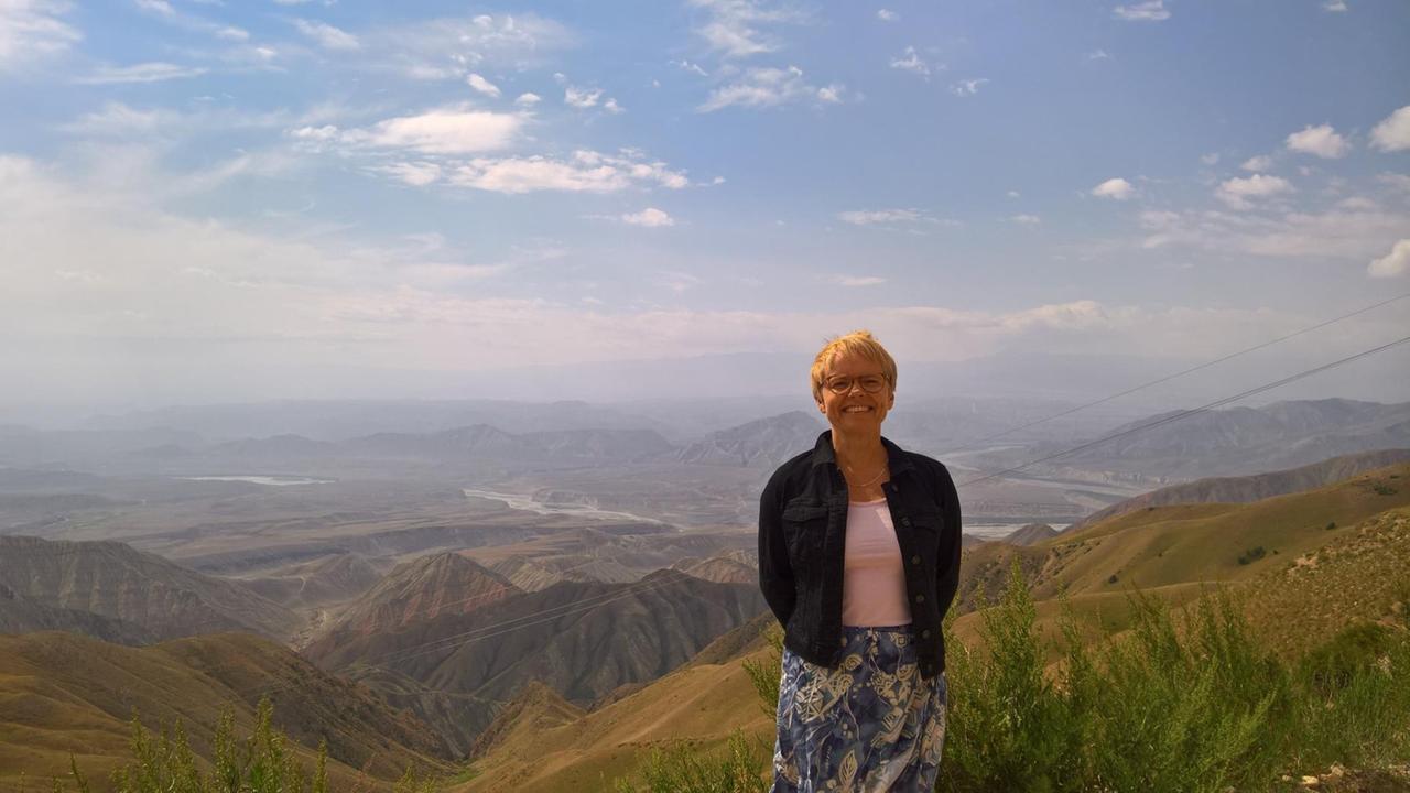 Reporterin Margarete Wohlan im Tian Shen im Norden von Kirgistan. Sie steht auf einem Berg, hinter ihr eine Bergkette.